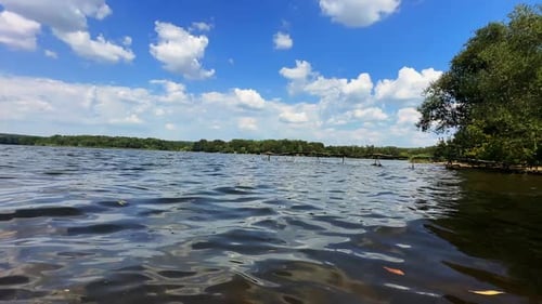 Wellenförmige Oberfläche des Flusses mit einigen schwimmenden Blättern. Bäume am Wasser vor dem Hintergrund des blauen Himmels