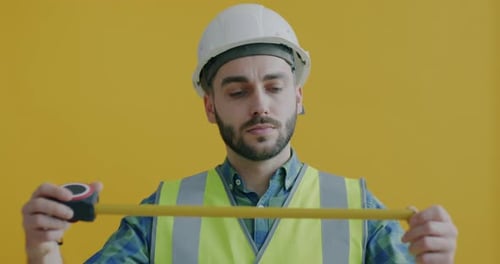 Portrait of Builder in Uniform Using Tape Measure Standing on Yellow Background Alone