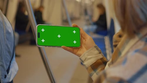 Madre mostrando un teléfono inteligente con pantalla verde en el metro