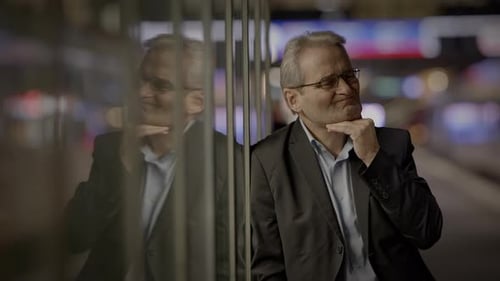 A Businessman Alone at Night Reflecting in the Glass of a Modern Office Building in the City