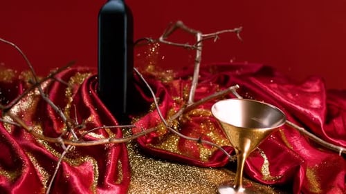 Crashing the table of of gilded wine bottle, paired with a bottle and vibrant red fabric on the tabl