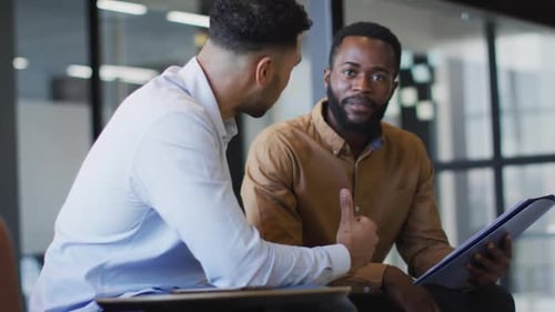 Video of two diverse businessmen discussing document at office meeting