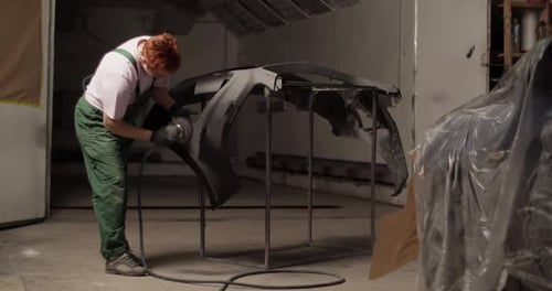 Repairwoman Sanding Bumper Near Vehicle