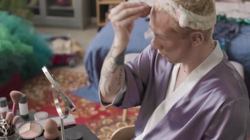 Hombre queer se aplica un escultor en la cara mientras se prepara para un espectáculo de drag