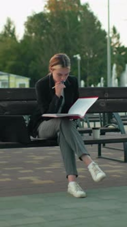 Student Reading Book Outdoors with Laptop and Coffee in Urban Park Setting