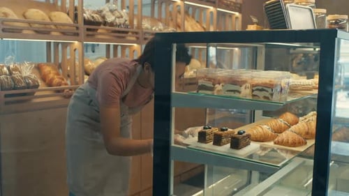 Female Worker Putting Desserts on Display Shelf in Bakery