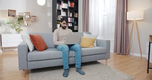 Man Works on Laptop at Home on Couch