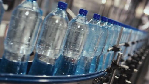 Flaschen mit stillem Wasser oder Tafelwasser, das auf einer Roboterförderlinie bewegt wird