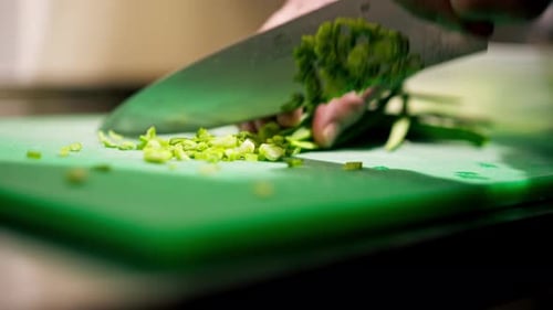 Closeup in the Kitchen on a Green Board the Process of Cutting Greens with Knife