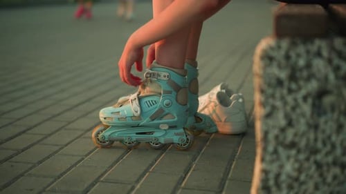 Une dame retire sa sangle de patin à roulettes alors qu'elle est assise sur le trottoir au coucher du soleil