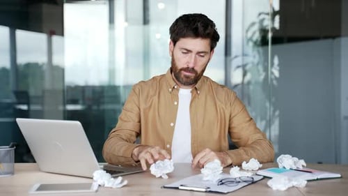 Exhausted bearded businessman is bored sitting at workplace at desk in business office. Overworked