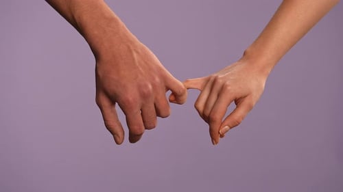 Man and Woman Holding Hands Touching with Pinky Fingers Holding in Lock Isolated on Purple Studio