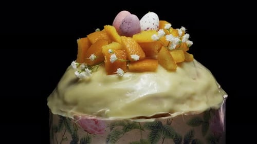 Osterkuchen mit Orange, kleinen Eiern und weißen Blumen auf schwarzem Hintergrund. Dreht sich in Nahaufnahme.