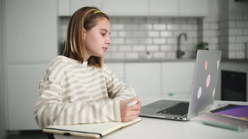 Girl Writing in Notebook with Laptop in Kitchen