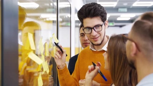 Business Team Brainstorm Writing Ideas on Paper Sticky Notes and Post It on Glass Wall Startup