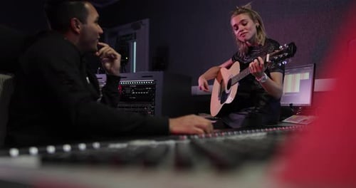 Woman plays guitar with man in recording studio