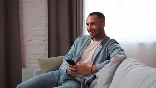 Young Adult Using Smartphone on Sofa at Home