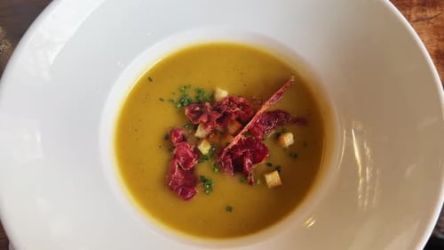Pumpkin Cream Soup with Jamon Herbs and Croutons on a Wooden Table in a Restaurant