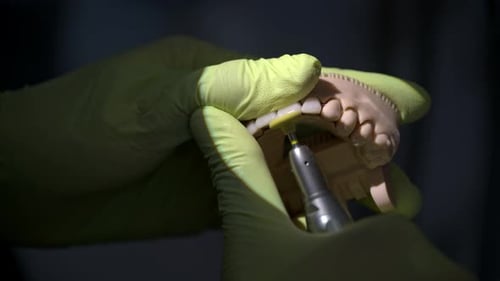 Slow motion shot of a dentist wearing green latex gloves filing a set of ceramic composite veneers o