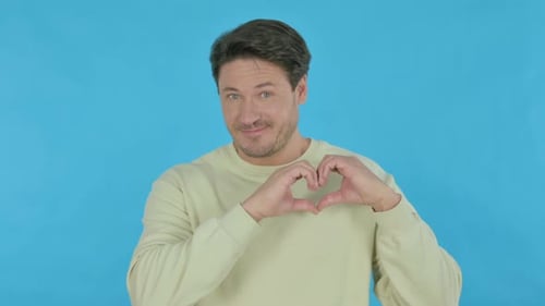 Smiling Man Gestures Heart on Blue Background