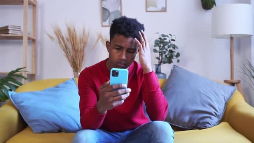 Worried Man Looking at Phone on Sofa