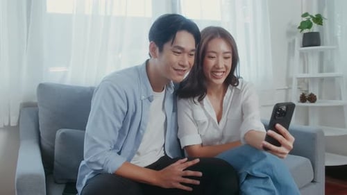 Young smiling asian couple holding smartphone and making video call at home