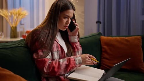 Femme multitâche caucasienne étudiant, parlant, téléphone portable, écrivant des notes à la maison, soirée en ligne