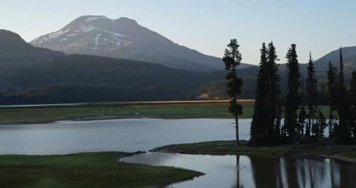 Lago de montanha tranquilo com floresta alpina e picos nevados distantes