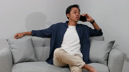 Man Relaxing on Sofa Chatting on Mobile Phone