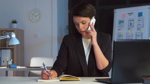 Woman on Phone Taking Notes in Office at Night