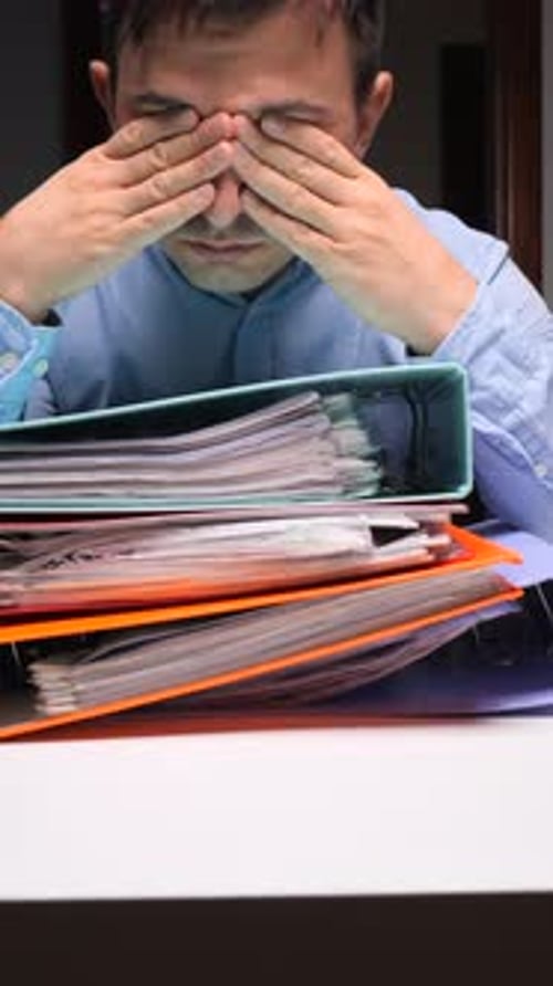 Stressed Man with Paperwork at Desk Indoors