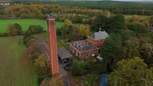 Wide Aerial Perspective of Old Water Pumping Station Surrounded by Autumn Woodland in Near
