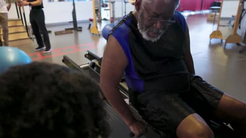 Senior Man Works with Trainer on Exercise Machine