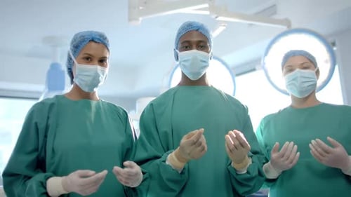 Portrait of three diverse male and female surgeons in operating theatre, slow motion