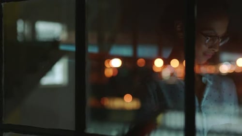 Black woman in business and thinking on tablet in office, working at night while looking at city
