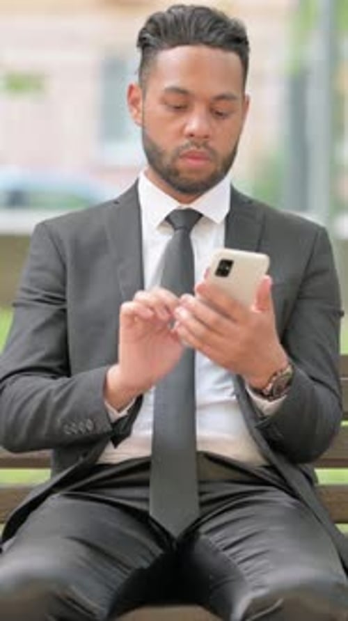 Man in Suit Using Phone While Sitting Outdoors