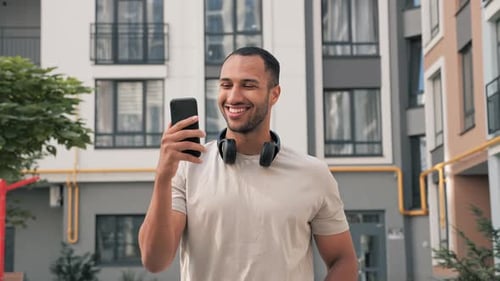 Smiling Man Video Chatting in Front of Apartment Building