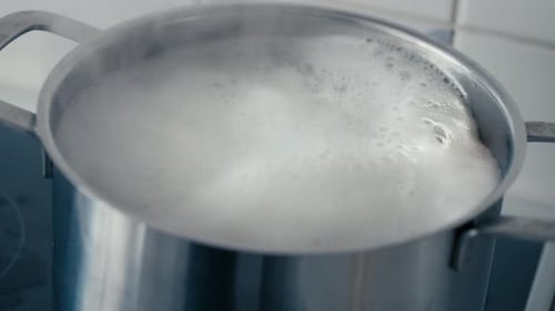 Close up of Boiling Water with Pasta in a big steel Pot on the Stove bubbling and steaming in slow m