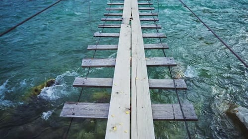 A Scenic and Beautiful Wooden Suspension Bridge Gracefully Arches Over the Clear Blue Sparkling
