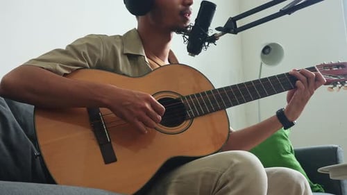 Close-up of musician's hands on guitar while records song in living room