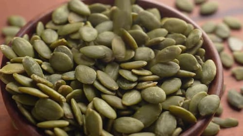 Green fresh Pumpkin seeds are dropping into a wooden bowl.