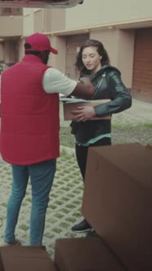 Man Hands Parcel to Woman on Street Corner Delivery Person Offers Package As Woman Signs and