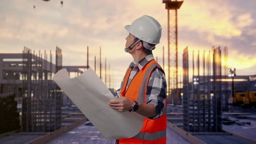 Seitenansicht eines asiatischen männlichen Ingenieurs, der auf der Baustelle den Bauplan in seinen Händen betrachtet