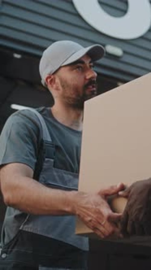 Portrait of Worker Giving Cardboard Box to African American Colleague for Delivery Looking at Camera