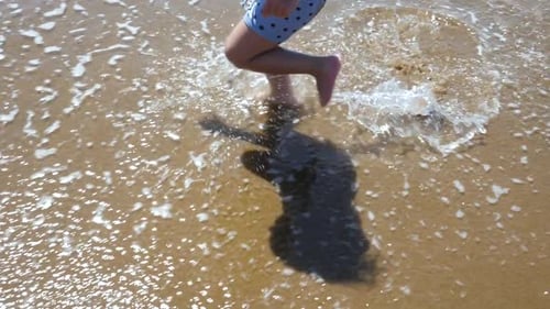 Close-up of a three-year-old boy's feet running along the beach and splashing in the waves in slow m