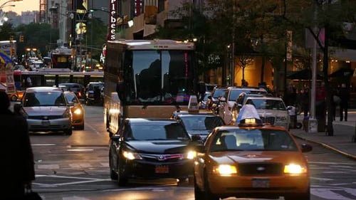 Pedestrians and cars flowing through the streets of New York City at sunset