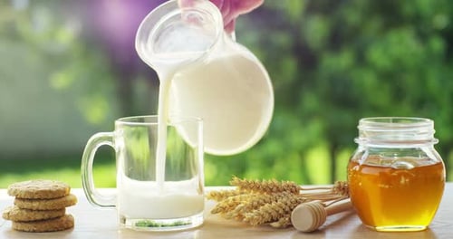 the hand of a boy on a sunny day in the garden pours milk in a transparent cup concept of healthy
