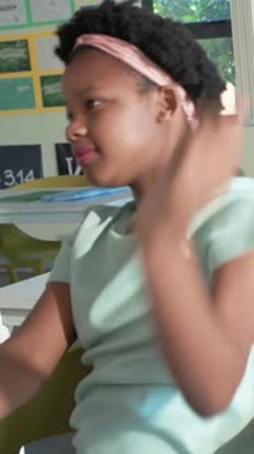 Vertical video: Responding to class cue kid raising, smiling at school desk, mint shirt, copy space