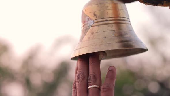 Close up of hands ringing bell at temple sanctum during puja or worship ...