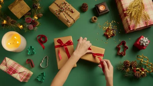 Overhead View of Woman Tying Red Silk Ribbon on Golden Gift Box Top Down